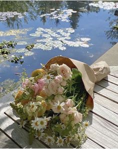 a bouquet of flowers sitting on top of a wooden table next to water and lily pads