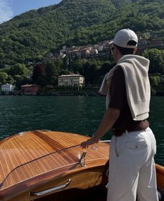 a man standing on top of a boat in the water next to a lush green hillside