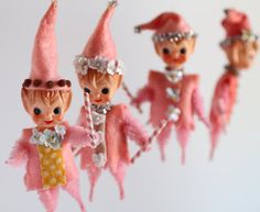 three little figurines are hanging from strings with pink hair and clothes on them