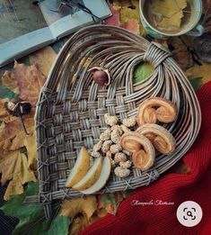 a wicker heart shaped basket filled with apples, cinnamons and nuts next to an open book