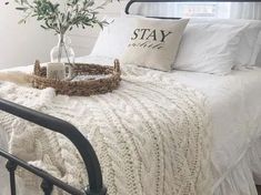 a bed with white blankets, pillows and a basket on top of it next to a window