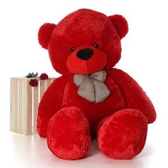 a large red teddy bear sitting next to a gift box