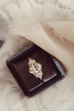 an engagement ring sitting on top of a black box next to a white lace cloth