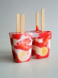 two popsicles with strawberries and banana slices in them, sitting next to each other