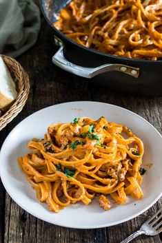 a white plate topped with pasta next to a skillet filled with meat and cheese