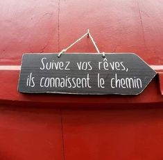 a black sign hanging from the side of a red building that says, suivez vos reves, its connaisent le chemin