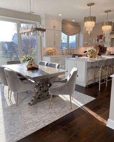 a dining room table and chairs in front of an open kitchen with lots of windows