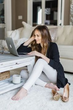 a woman is sitting on the floor with her laptop and shoes in front of her