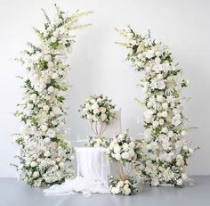 two tall white flowers are next to each other on a table with an arch made out of them