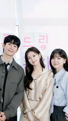 three young people standing next to each other in front of a wall with korean characters on it