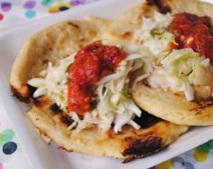 two tortillas with sauce and shredded cabbage on a white plate, sitting on a colorful tablecloth