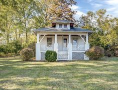 a small white house sitting on top of a lush green field in front of trees