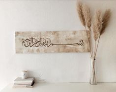 a vase filled with dry grass sitting on top of a white table next to a book