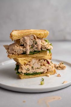 two sandwiches stacked on top of each other with meat and vegetables in the middle, sitting on a white plate