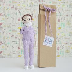 a crocheted doll sitting next to a brown paper bag with a purple ribbon