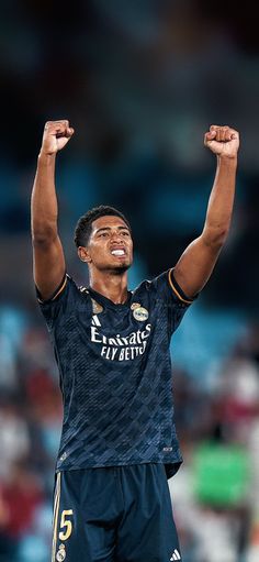 a soccer player raising his arms in the air with one hand up and two hands raised above his head