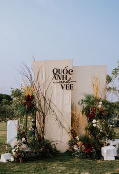 an outdoor wedding ceremony setup with flowers and greenery on the grass, in front of a white backdrop