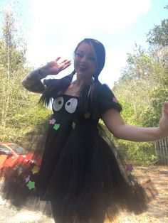 a woman in a black dress is smiling and waving her arms out to the side