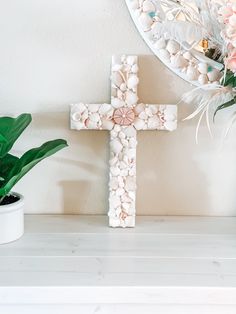 a white cross sitting on top of a table next to a potted plant and mirror