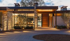 the entrance to a modern home with stone and wood accents at night time, lit up by outdoor lighting