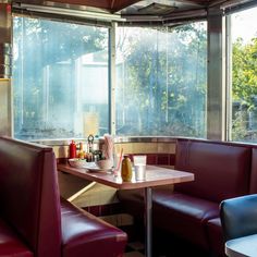 two booths with red leather seats in front of large windows and trees outside the window