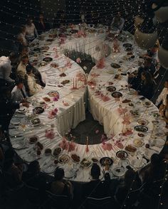 a group of people sitting around a round table with plates and candles on it,