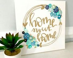 a white sign that says home is where the heart is on it next to a potted plant