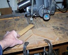 a person working on a piece of wood with a machine in the background and another hand holding something near it