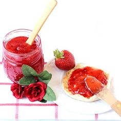 a strawberry jam in a jar next to a spoon and some strawberries on a plate