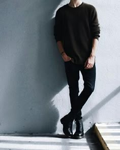 a young man leaning against a wall with his hands in his pockets and shoes on