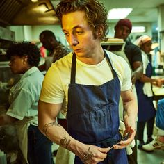 a man with tattoos on his arm standing in front of other people wearing aprons