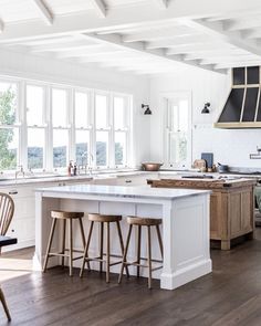 a kitchen with an island and two stools next to the counter top in front of large windows