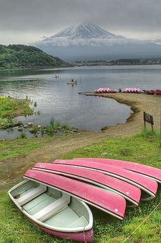 two canoes are on the grass next to a body of water with a mountain in the background