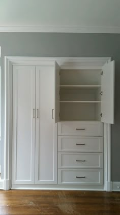 an empty room with white cupboards and drawers on the wall next to hardwood flooring