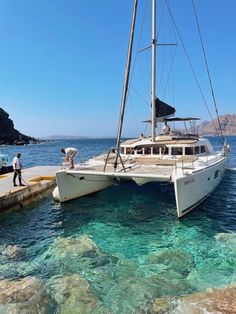 two people standing on the dock next to a catamaran in clear blue water