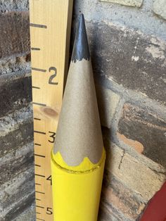 a wooden ruler with a yellow pencil in it next to a gray and yellow cone