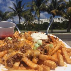 a white plate topped with french fries covered in cheese and chili next to a cup