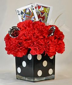 red carnations and white polka dots in a black vase with playing cards on top