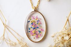 a necklace with flowers in it sitting on a table next to some dried grass and white flowers