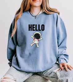 Embrace the wonders of the cosmos with this "Hello from the Cosmos" Sweatshirt. Featuring a charming little astronaut waving a friendly Hello, this crewneck is perfect for space enthusiasts and dreamers alike. The playful design captures the adventurous spirit of exploration, bringing a touch of the galaxy to your everyday wardrobe. Whether you're an Earthling or just visiting from other planet, this shirt offers a cosmic greeting that's out of this world.  ♥ PRODUCTION TIME: 1-5 days (Usually 2 Cheap Space-themed Crew Neck Tops, Space Sweatshirt, Astronomy Gifts, Trust The Universe, Galaxy Shirt, Astronomy Gift, Space Shirts, Statement Fashion, Nasa Space