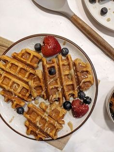 waffles and strawberries on a plate next to bowls of berries, blueberries and cinnamon sticks