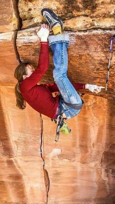 a woman climbing up the side of a cliff with her feet in the air while holding onto a rope