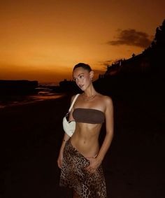 a woman standing on top of a sandy beach next to the ocean at night with an orange sky in the background