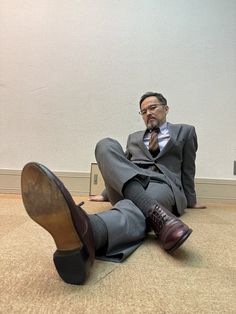 a man in a suit and tie sitting on the floor with his foot up to his shoe