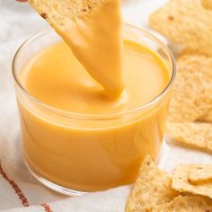 a person dipping cheese into a small glass bowl with crackers on the table next to it