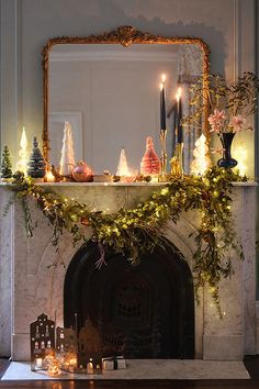 a mantel decorated with candles and greenery in front of a mirror on top of a mantle