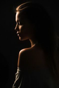 a woman standing in the dark with her hair blowing back and looking off to the side