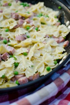 pasta with ham and peas in a skillet on a checkered tablecloth, ready to be eaten