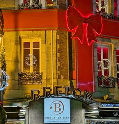 the front of a building decorated with christmas lights and decorations, including a large red bow