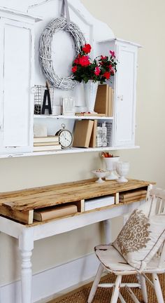 a white desk with flowers and books on it next to a wall mounted shelf filled with books